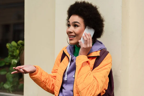 Femme afro-américaine joyeuse parlant sur smartphone près du bâtiment à l'extérieur — Photo de stock