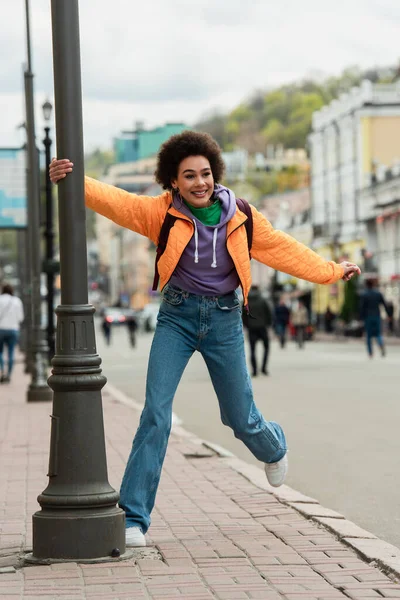 Mujer afroamericana feliz de pie cerca de la linterna en la calle urbana - foto de stock