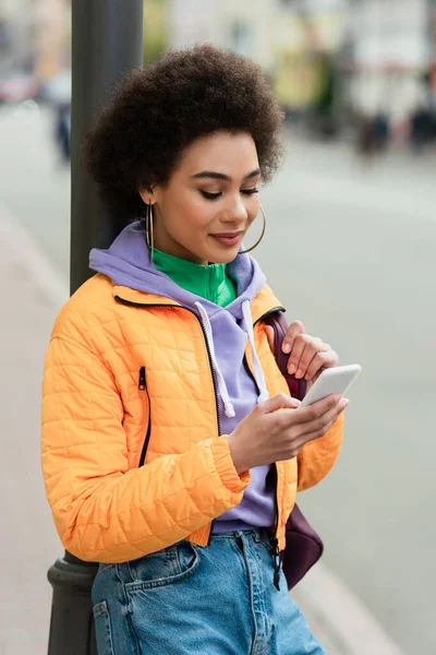 Досить африканська американка з рюкзаком, який користується мобільним телефоном на міській вулиці. — стокове фото