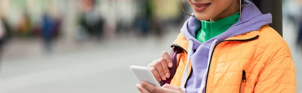 Ausgeschnittene Ansicht einer lächelnden Afroamerikanerin mit Handy im Freien, Banner — Stockfoto