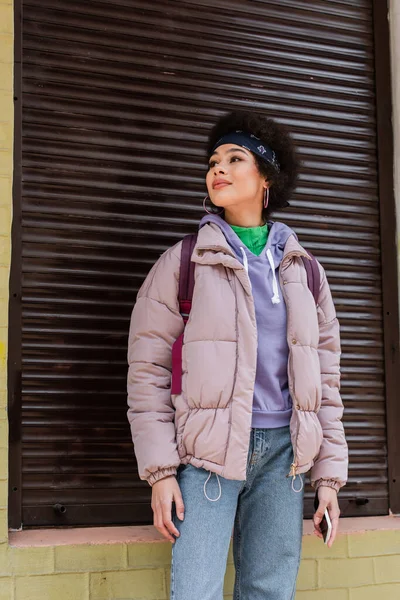 Hübsche Afroamerikanerin mit Handy steht neben Gebäude mit Rollladen — Stockfoto
