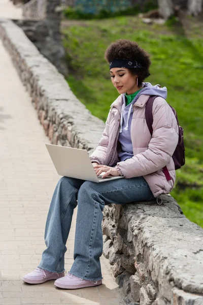 Jovem afro-americana usando laptop no parapeito no parque — Fotografia de Stock