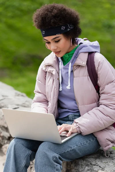 African american teleworker using laptop on parapet in park — Stock Photo