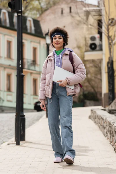 African american woman with laptop walking on urban street — Stock Photo