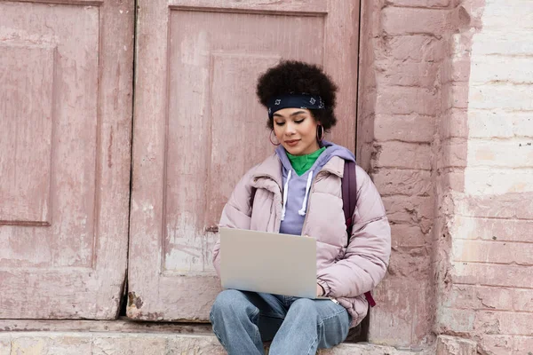 African american freelancer in jacket using laptop near building — Stock Photo