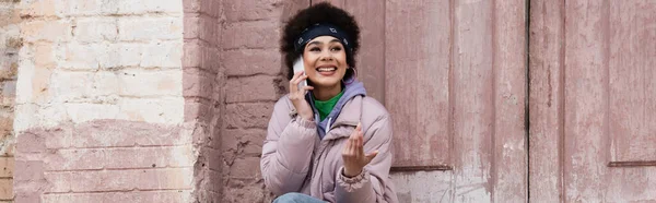 Femme afro-américaine joyeuse parlant sur un téléphone portable près du bâtiment, bannière — Photo de stock