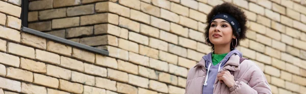 Африканская американка в пиджаке, стоящая возле здания с кирпичным фасадом стены, баннер — стоковое фото