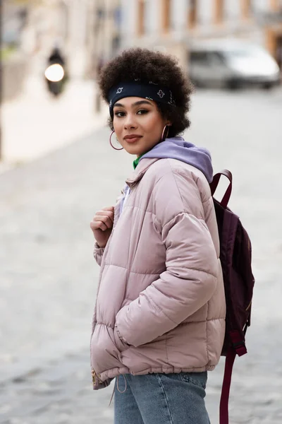 African american woman in jacket holding backpack on urban street — Stock Photo