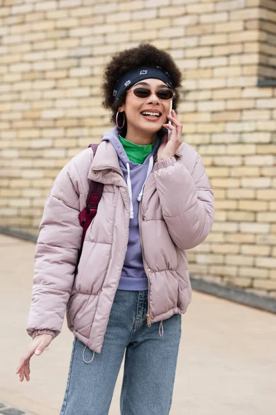 Fröhliche afrikanisch-amerikanische Frau mit Sonnenbrille spricht draußen auf dem Smartphone — Stockfoto