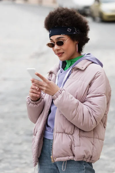 Mulher afro-americana em bandana e óculos de sol usando smartphone ao ar livre — Fotografia de Stock