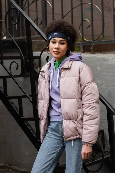Donna afroamericana in giacca guardando la fotocamera vicino alle scale sulla strada — Foto stock