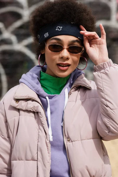 Mujer afroamericana sonriente en gafas de sol y pañuelo de pie al aire libre - foto de stock