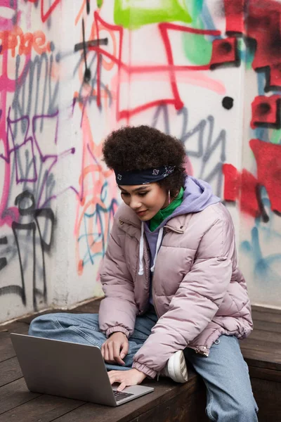 African american freelancer using laptop near graffiti on wall — Stock Photo