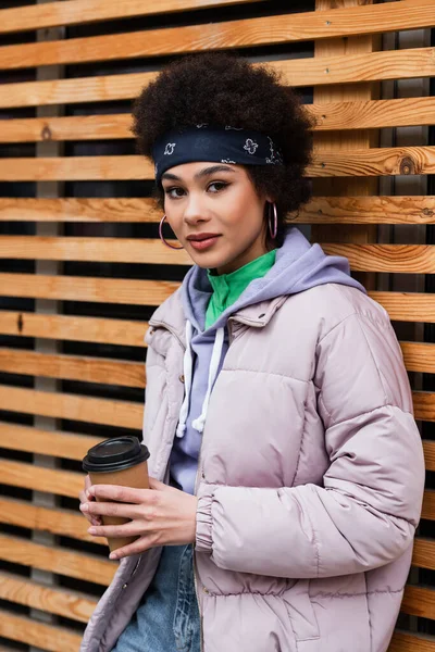 Pretty african american woman in bandana holding paper cup near wooden fence — Stock Photo