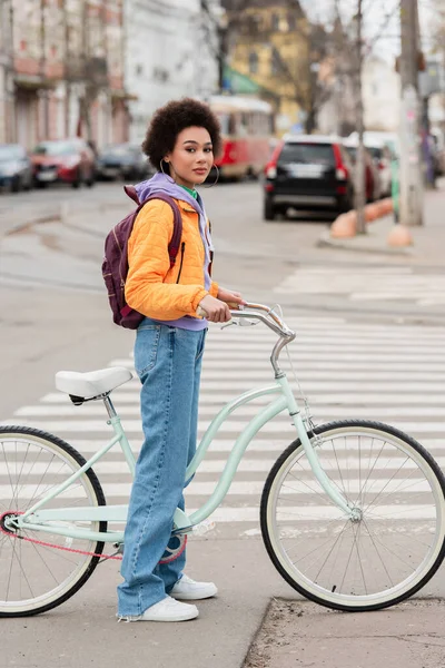 Young african american woman standing near bike on road on urban street — Stock Photo