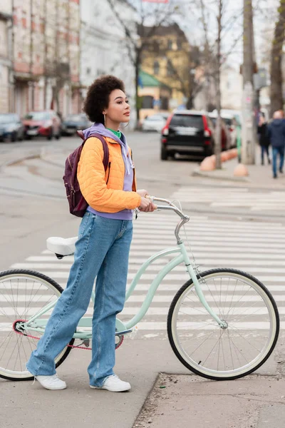 Jovem afro-americana de pé perto de bicicleta e passarela ao ar livre — Fotografia de Stock