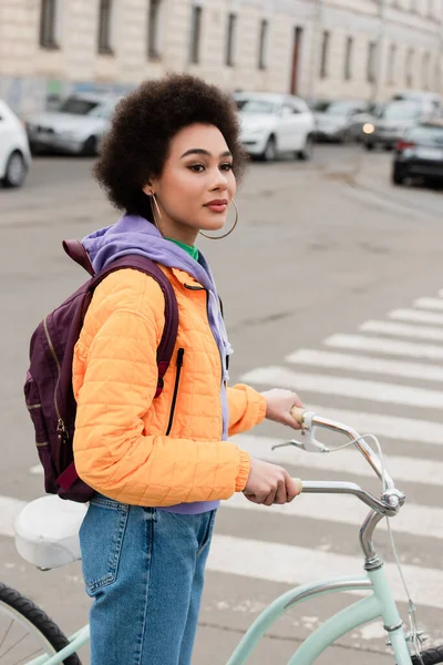 Femme afro-américaine avec vélo regardant loin près de passages piétons flous à l'extérieur — Photo de stock