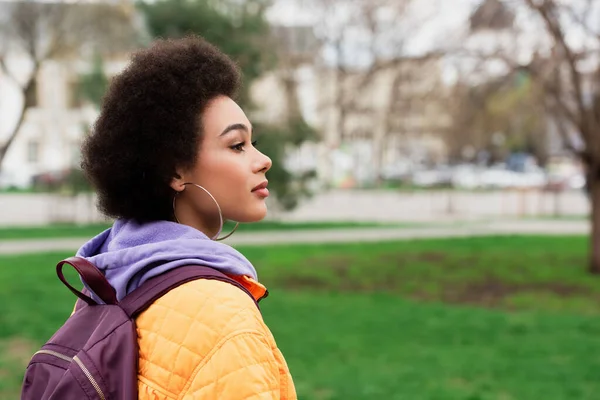 Vista lateral da mulher americana africana bonita com mochila em pé ao ar livre — Fotografia de Stock