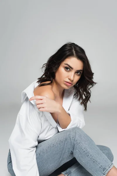 Brunette woman taking off shirt on grey background — Stock Photo