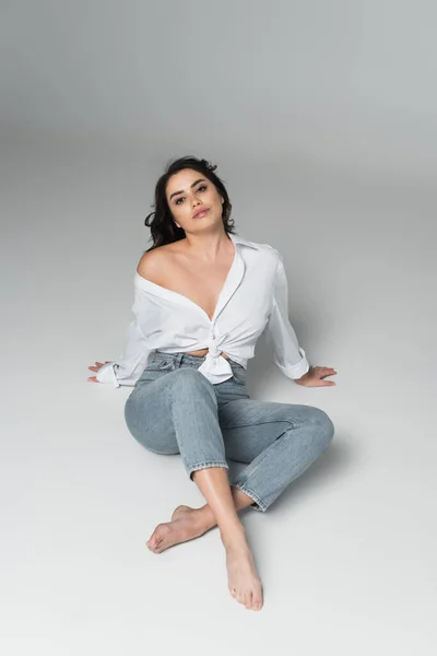 Vista de alto ángulo de mujer sexy y descalza en jeans sobre fondo gris - foto de stock