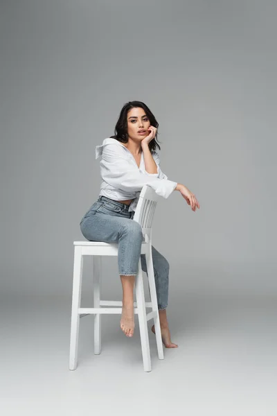 Femme séduisante assise sur une chaise sur fond gris — Photo de stock