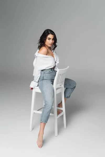 Sensual barefoot woman in shirt posing on chair on grey background — Stock Photo