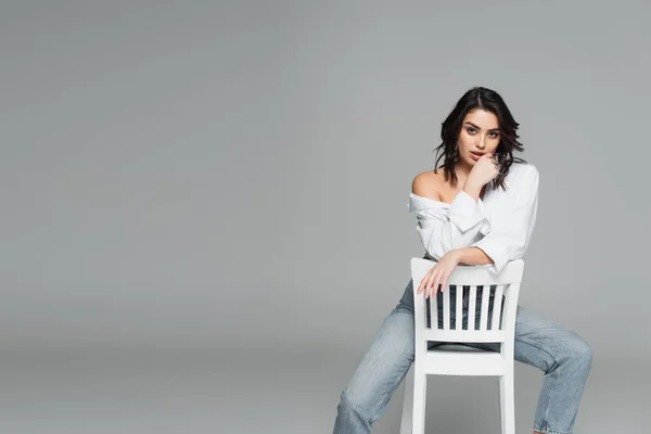 Sinnliche Frau posiert auf weißem Stuhl isoliert auf grau — Stockfoto