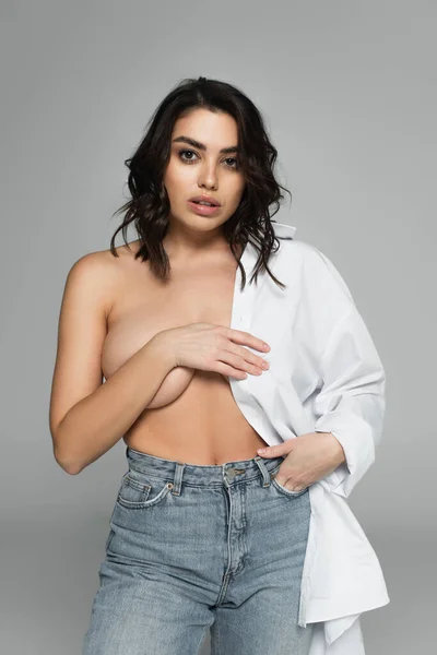Mulher sexy com peito nu segurando mão no bolso de jeans isolado em cinza — Fotografia de Stock