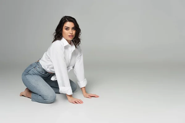 Sinnliche Frau im weißen Hemd kniet auf grauem Hintergrund — Stockfoto