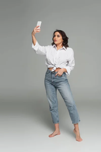 Donna sexy scattare selfie su smartphone su sfondo grigio — Foto stock