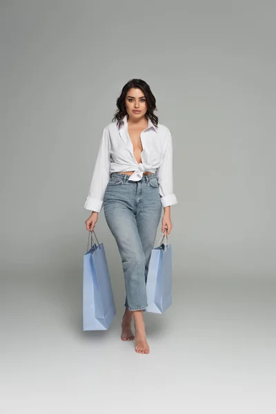 Sexy Frau im weißen Hemd mit Einkaufstaschen auf grauem Hintergrund — Stockfoto
