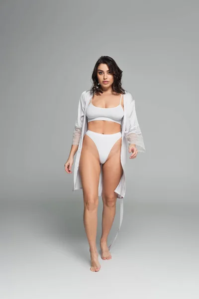 Mujer morena bonita en ropa interior y bata de seda sobre fondo gris - foto de stock