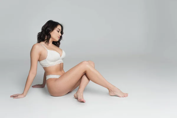 Vue latérale de la femme sexy en dentelle blanche sous-vêtements assis sur fond gris — Photo de stock