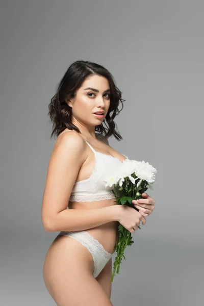 Sensual woman in lingerie holding bouquet and looking at camera isolated on grey — Stock Photo