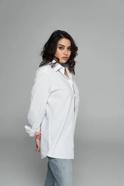 Brunette woman in jeans and shirt standing isolated on grey — Stock Photo