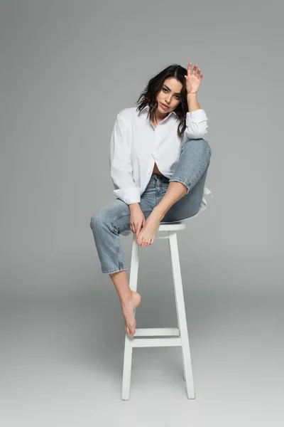 Jeune femme brune assise sur une chaise sur fond gris — Photo de stock