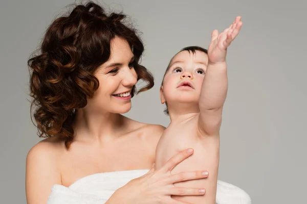 Happy mother with bare shoulders holding in arms son with outstretched hand isolated on grey — Stock Photo