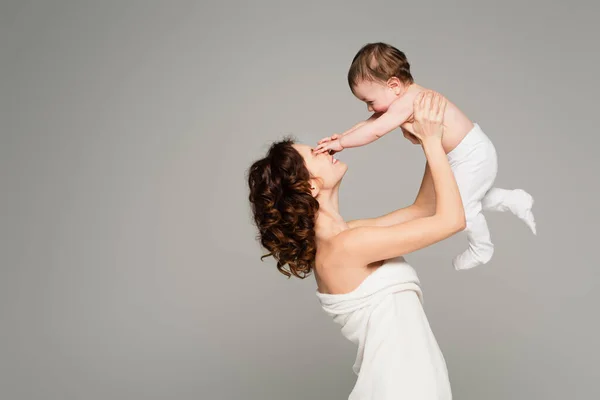 Niño en medias de bebé tocando la cara de madre feliz en toalla aislada en gris - foto de stock