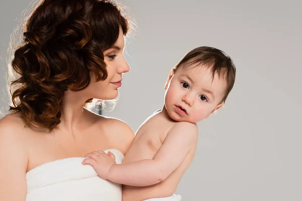 Lockige Mutter mit nackten Schultern, die ihren kleinen Sohn in den Armen hält, isoliert auf grau — Stockfoto