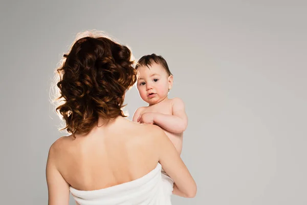 Mère bouclée tenant tout-petit fils dans les bras isolé sur gris — Photo de stock