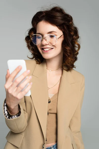 Happy woman in glasses and beige blazer taking selfie isolated on grey — Stock Photo