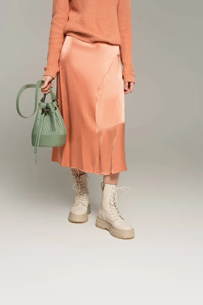 Cropped view of trendy woman in satin skirt holding bag on grey — Stock Photo