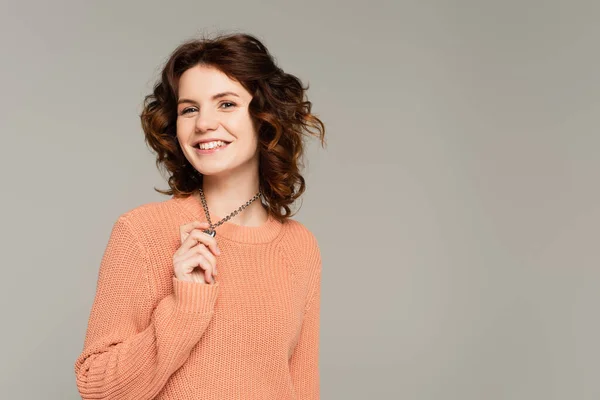 Positive woman in sweater holding necklace isolated on grey — Stock Photo