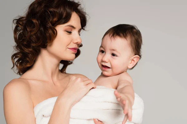 Caring mother with bare shoulders holding baby boy wrapped in towel isolated on grey — Stock Photo