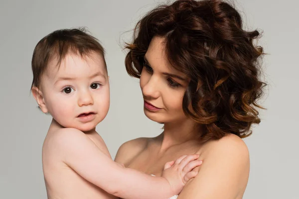Caring mother with bare shoulders looking at toddler son isolated on grey — Stock Photo