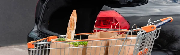 Einkaufswagen mit Einkäufen in der Nähe des offenen Kofferraums, Banner — Stockfoto