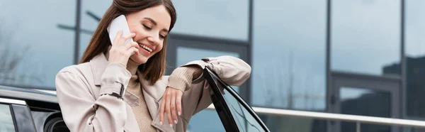 Cheerful young woman talking on cellphone near car outdoors, banner — Stock Photo