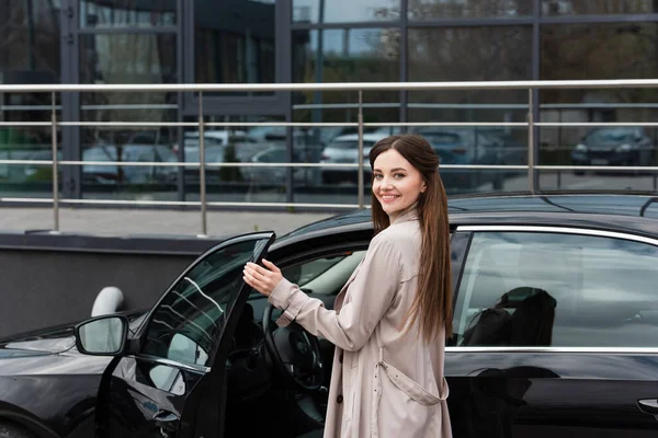 Mujer complacida sonriendo a la cámara al abrir la puerta del coche - foto de stock