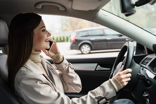 Side view of pleased woman talking on mobile phone while driving car — Stock Photo