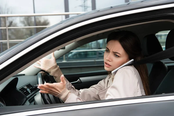 Серйозна молода жінка жестикулює під час розмови на смартфоні в машині — стокове фото